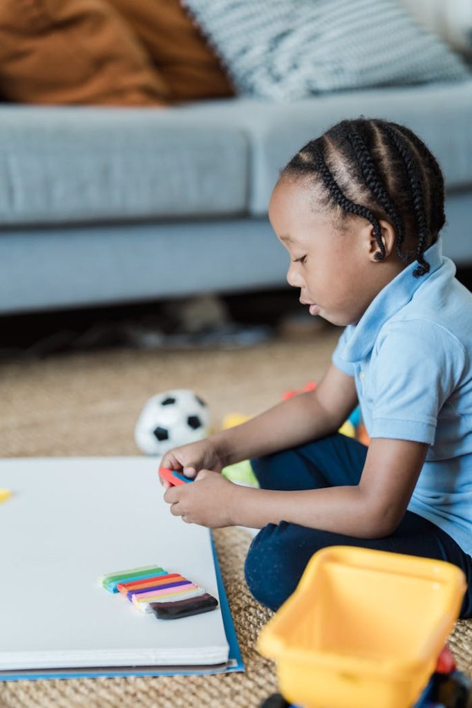 African American child playing with colorful plasticine on floor indoors, promoting creativity.
